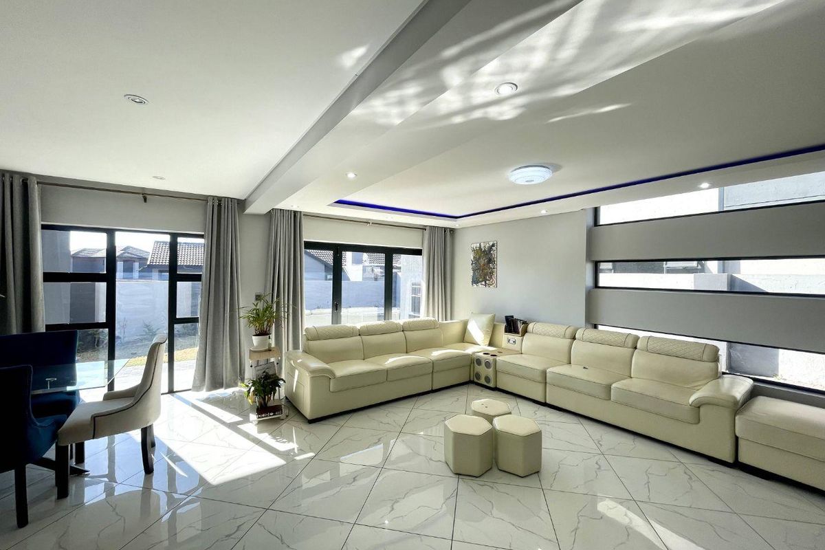 A bright and modern living room featuring large marble-look floor tiles, a sophisticated tray ceiling with recessed lighting, and expansive aluminium-framed windows and doors.