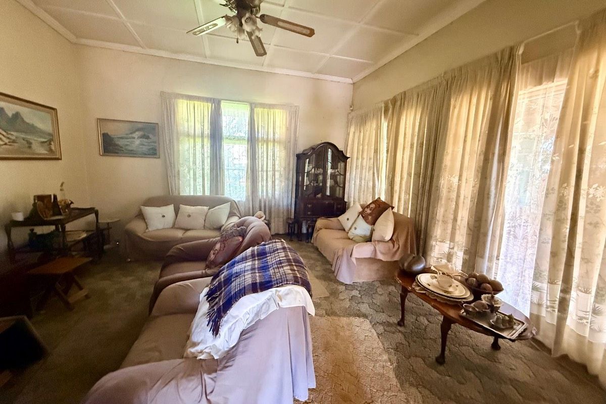 A spacious living room featuring large windows with natural light, a ceiling fan, and carpeted flooring, offering a traditional layout.