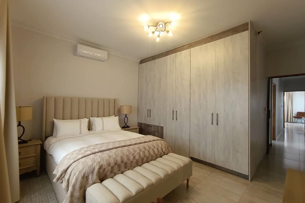A well-maintained bedroom featuring built-in floor-to-ceiling wardrobes, tiled flooring, and a wall-mounted air conditioning unit.
