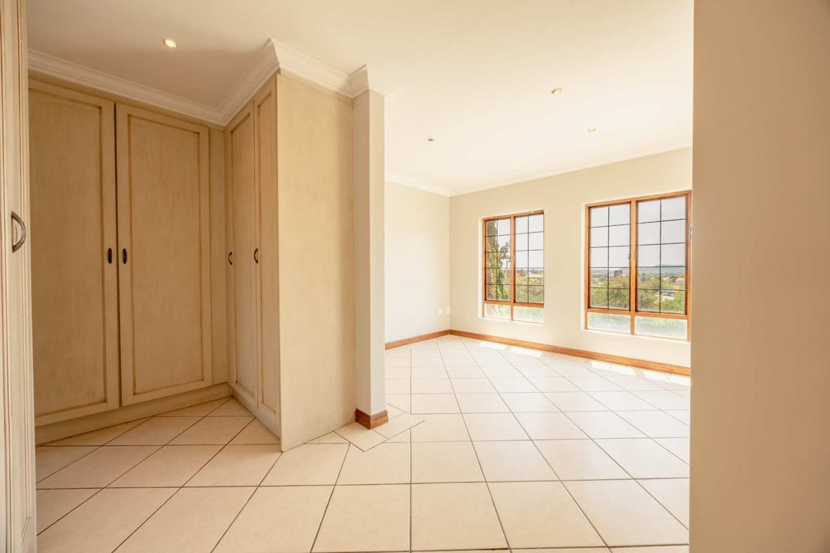 A spacious, sunlit bedroom featuring neutral tiled flooring, ample built-in cupboard storage, and large windows offering pleasant views.