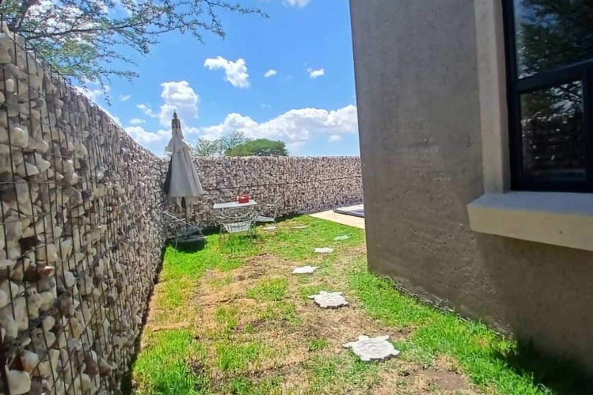 A side garden area featuring a decorative gabion stone wall, stepped stone pavers, and a stucco exterior wall finish.