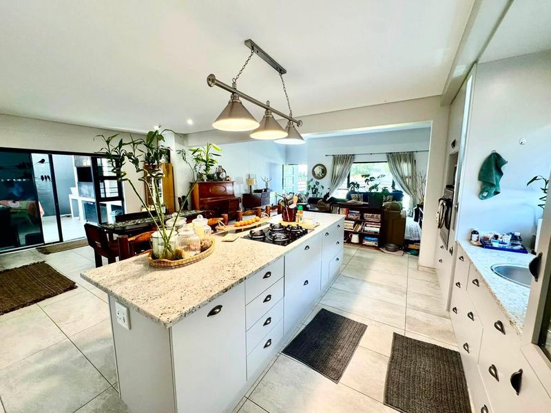 Spacious open-plan kitchen featuring a large central island with granite countertops, gas hob, and modern pendant lighting, seamlessly flowing into the living and dining areas.