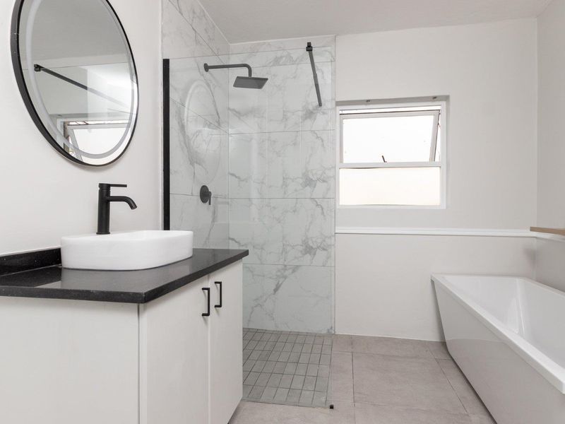 Modern bathroom featuring a sleek vanity with vessel sink, a spacious walk-in shower with marble-look tiling, and a contemporary freestanding bathtub.