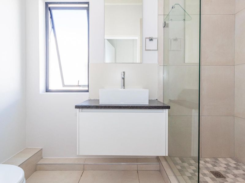 A clean, modern bathroom featuring a floating vanity with a vessel sink, a glass-enclosed shower, and neutral floor tiling.