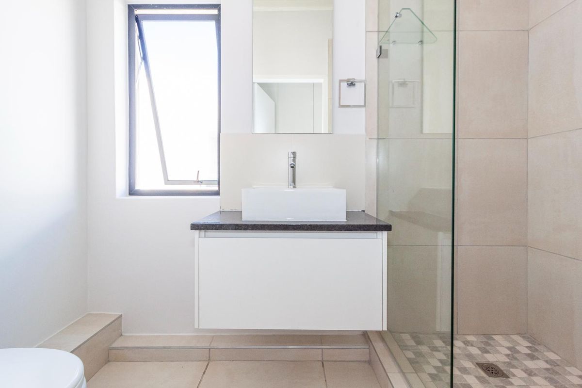 A clean, modern bathroom featuring a floating vanity with a vessel sink, a glass-enclosed shower, and neutral floor tiling.