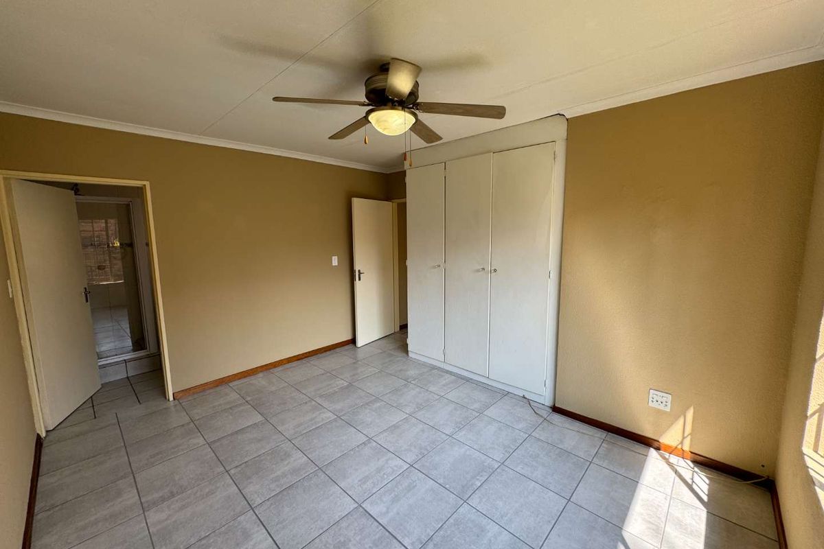 A spacious, empty bedroom featuring neutral wall tones, tiled flooring, a ceiling fan, and built-in storage cupboards.
