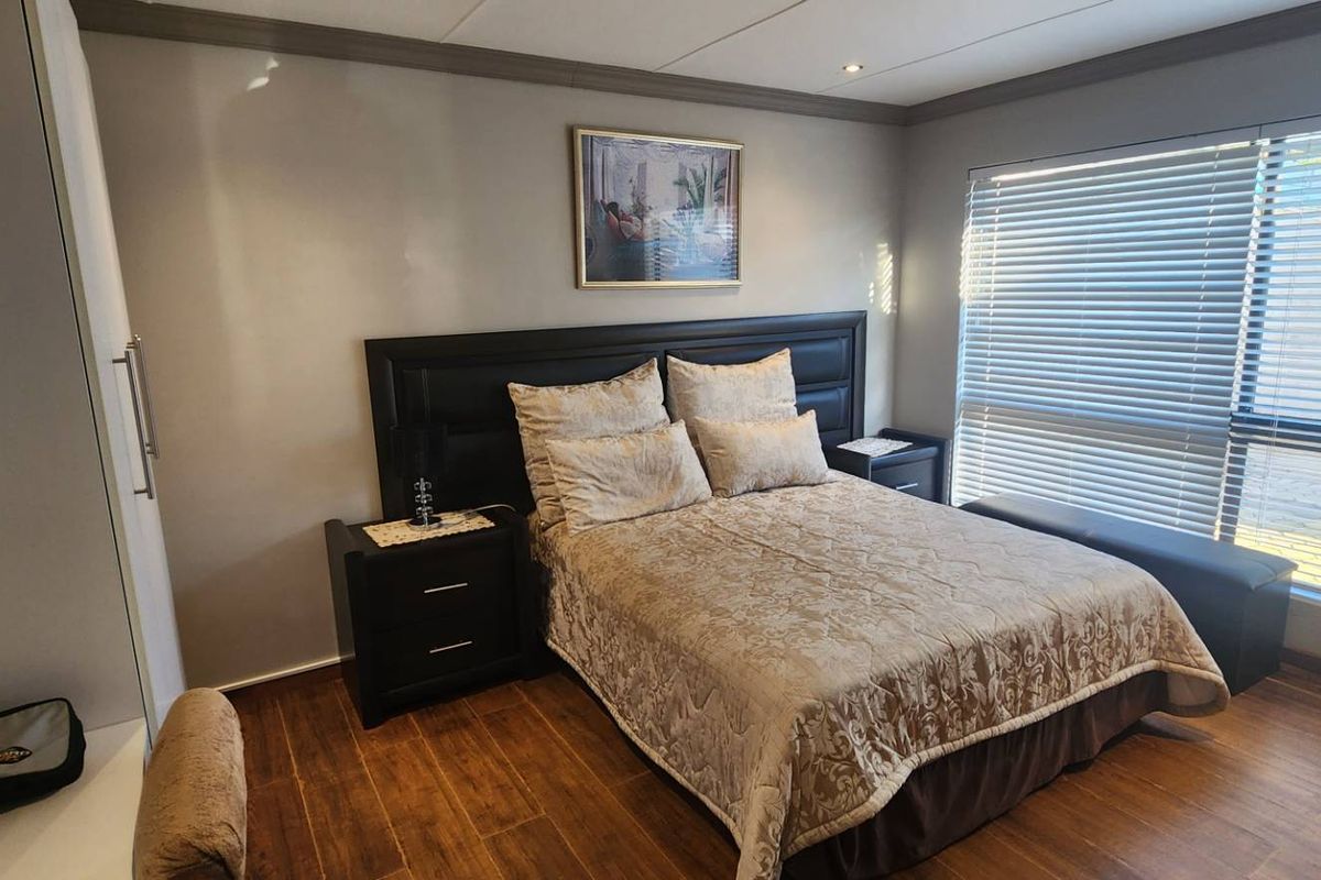 A well-maintained bedroom featuring wood-look flooring, built-in cabinetry, and large windows with fitted blinds, offering a comfortable and functional living space.