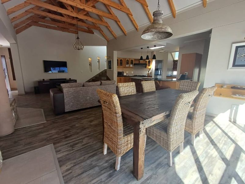 Spacious open-plan living and dining area featuring high vaulted timber-beamed ceilings, wood-look flooring, and a modern kitchen with integrated cabinetry.