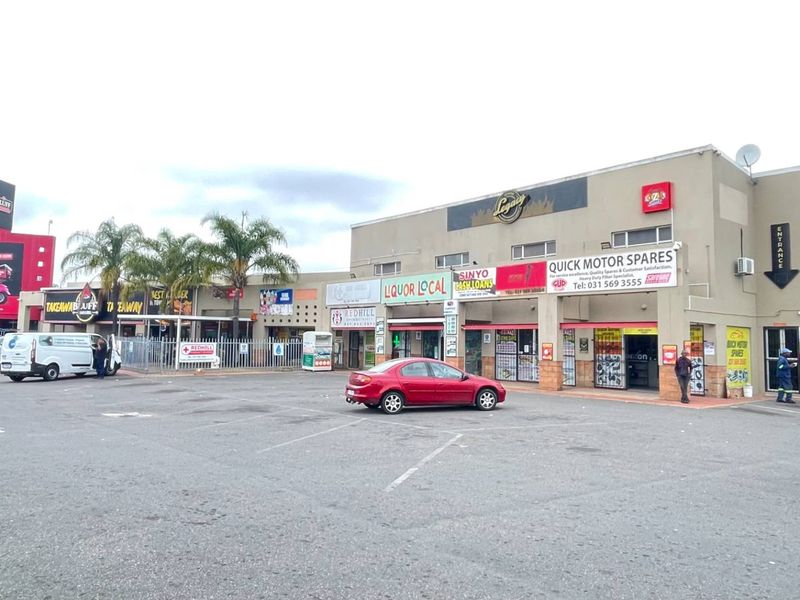 Front exterior view of a multi-tenant industrial and retail commercial complex featuring paved parking and various storefront signage.