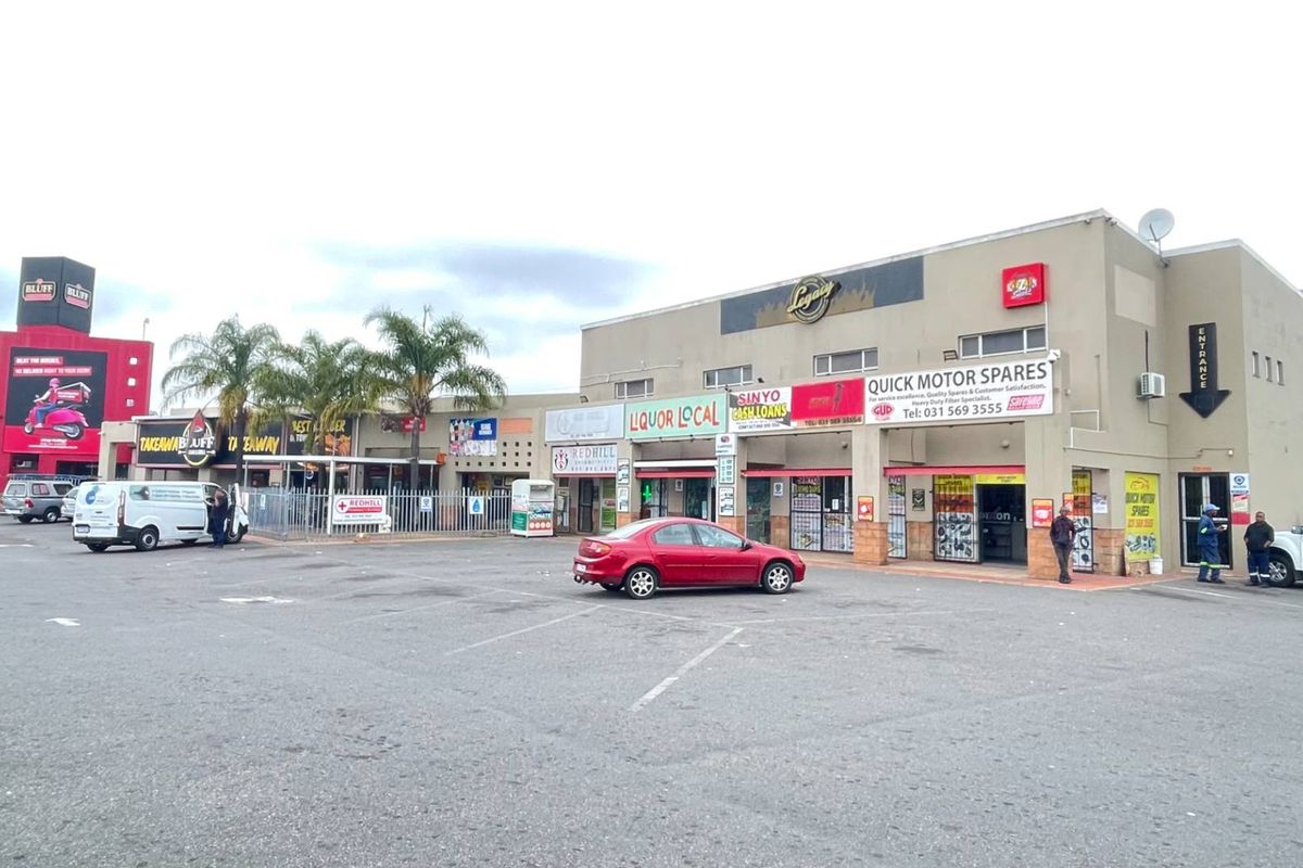 Front exterior view of a multi-tenant industrial and retail commercial complex featuring paved parking and various storefront signage.