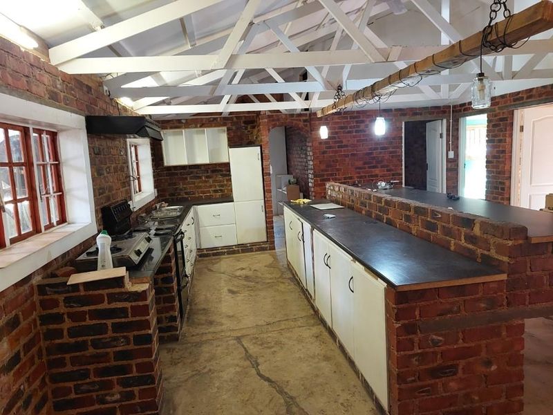 Rustic kitchen featuring exposed brick walls, timber roof trusses, and a large brick island, offering a unique industrial aesthetic with potential for modernization.