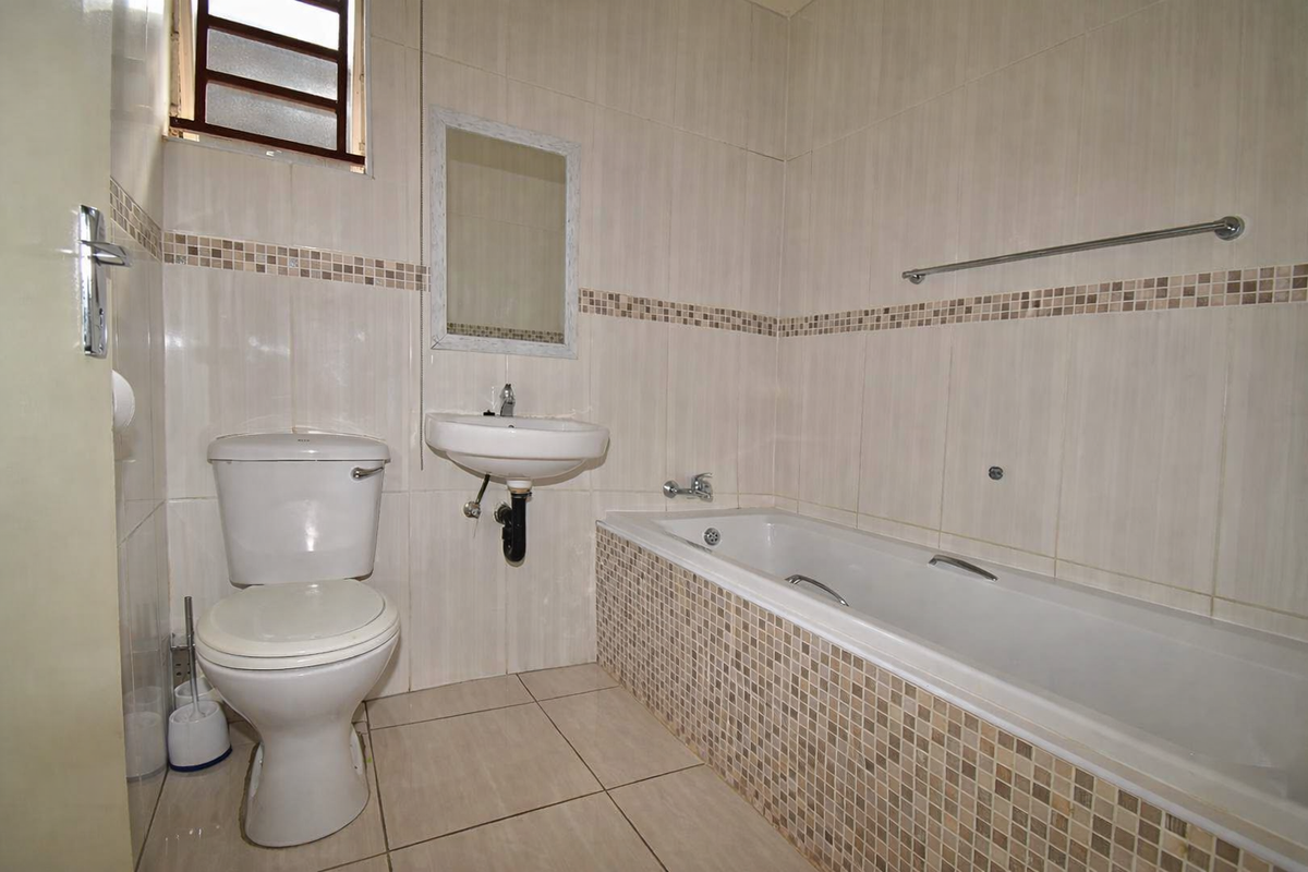 A functional bathroom featuring a bathtub, wall-mounted basin, and toilet with neutral wall and floor tiling.