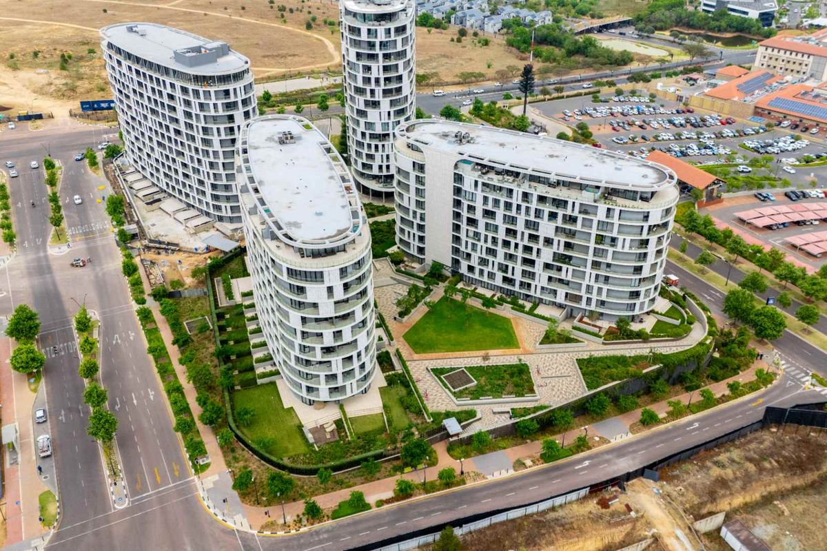 Aerial view of a modern apartment complex featuring multiple high-rise buildings, landscaped communal gardens, and paved pedestrian pathways within a secure estate.