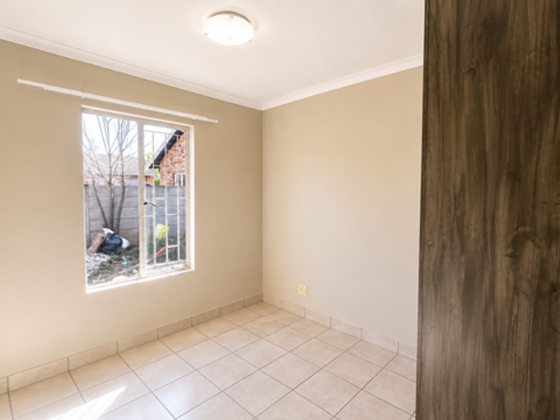A bright, empty bedroom featuring neutral wall tones, tiled flooring, and a built-in cupboard, offering a clean and versatile space.