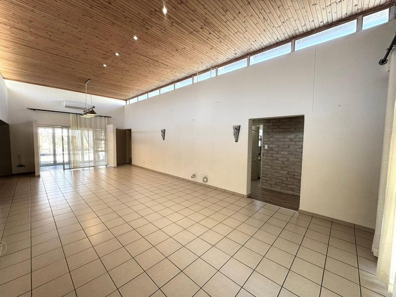 Spacious living area featuring a high timber-clad vaulted ceiling, clerestory windows for natural light, ceramic tiled flooring, and a unique brick-accented wall.