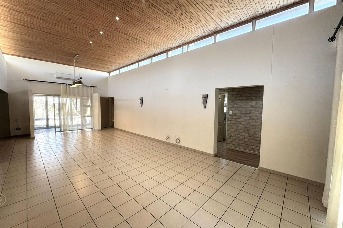 Spacious living area featuring a high timber-clad vaulted ceiling, clerestory windows for natural light, ceramic tiled flooring, and a unique brick-accented wall.