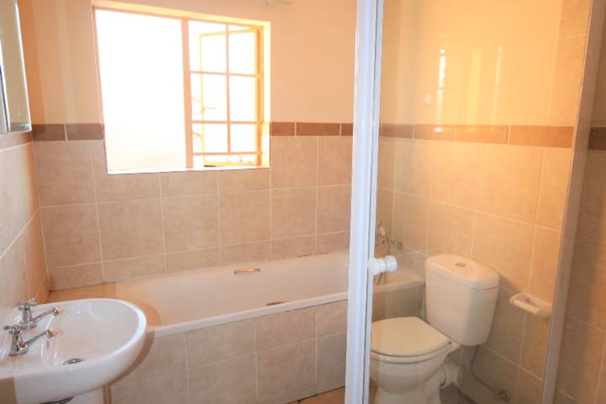 A functional bathroom featuring a pedestal basin, built-in bathtub, separate shower enclosure, and toilet with neutral tiled finishes.