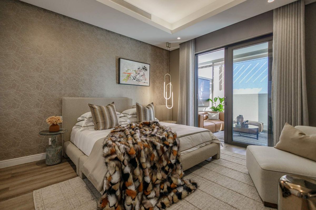 A modern, well-appointed bedroom featuring textured wallpaper, recessed ceiling lighting, and large sliding glass doors that open onto a private balcony.