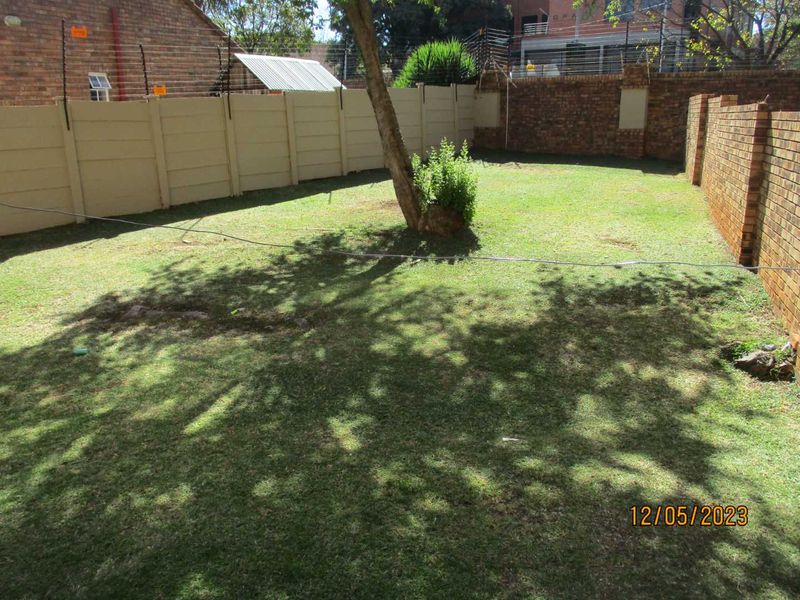 A private backyard garden featuring a lawn area enclosed by a combination of precast concrete and facebrick boundary walls with electric fencing.