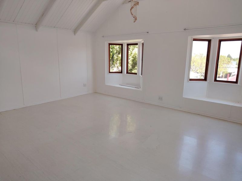 Spacious living area featuring a vaulted ceiling with exposed beams, painted timber flooring, and dual bay windows providing ample natural light.