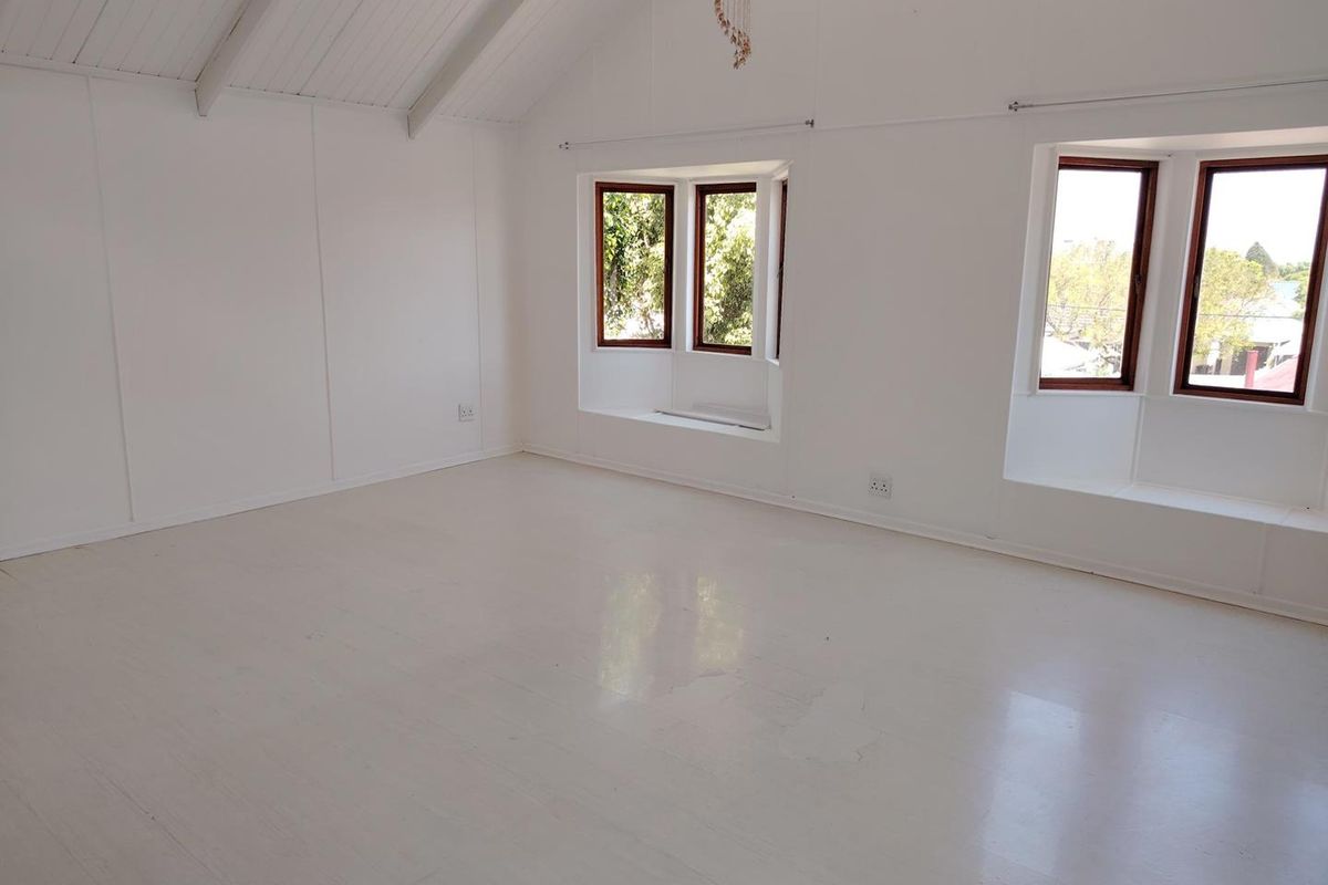 Spacious living area featuring a vaulted ceiling with exposed beams, painted timber flooring, and dual bay windows providing ample natural light.