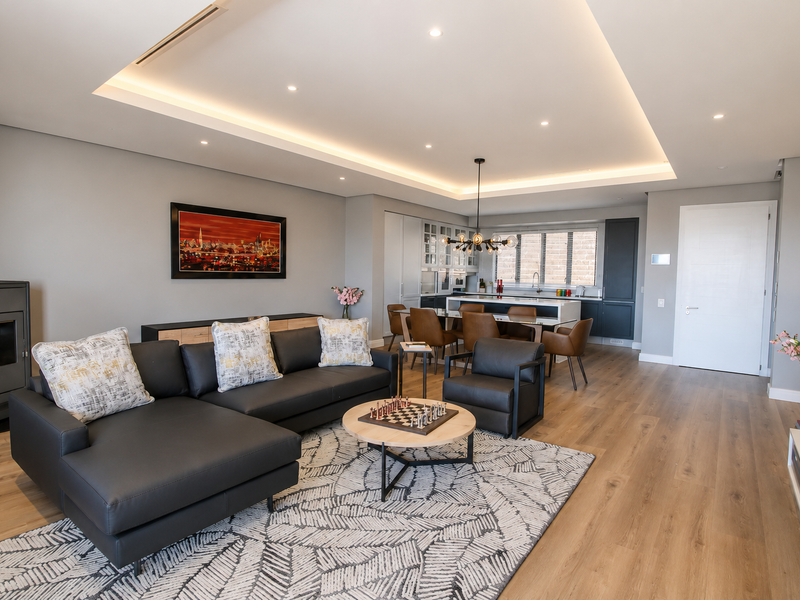 Spacious open-plan living and kitchen area featuring modern wood flooring, recessed cove lighting, a built-in fireplace, and a contemporary kitchen island.