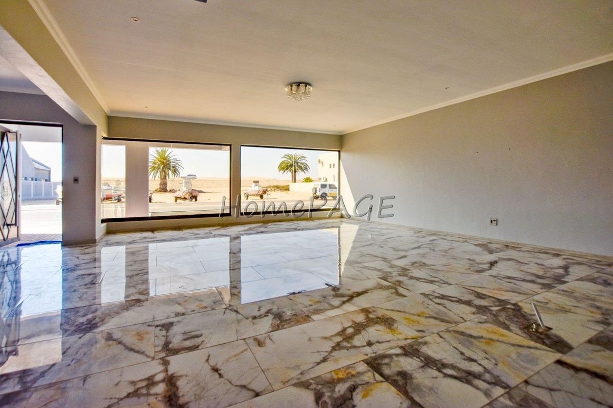 Spacious, empty living area featuring polished marble flooring, neutral walls, and large windows providing ample natural light and exterior views.