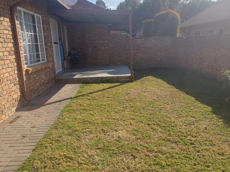A private rear garden featuring a brick-walled perimeter, a paved walkway, and a covered patio area attached to the townhouse.