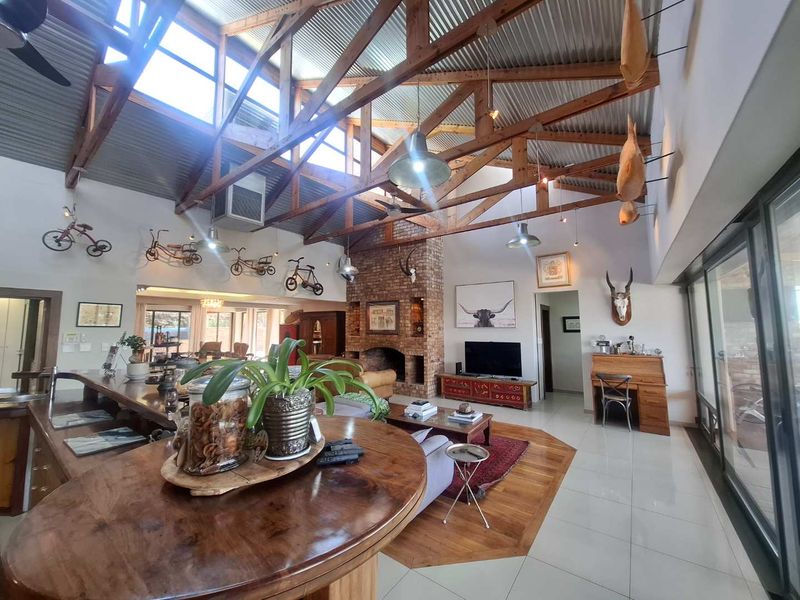 Spacious open-plan living area featuring high vaulted ceilings with exposed timber trusses, a prominent brick fireplace, and large sliding doors leading outdoors.