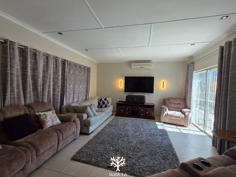A comfortable living room featuring tiled flooring, recessed ceiling lighting, a split-system air conditioner, and a sliding glass door providing natural light.