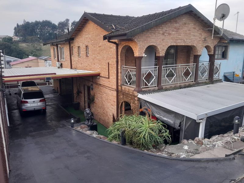 Front elevation of a double-story brick house featuring a covered carport, balcony with decorative metal railings, and a paved driveway.