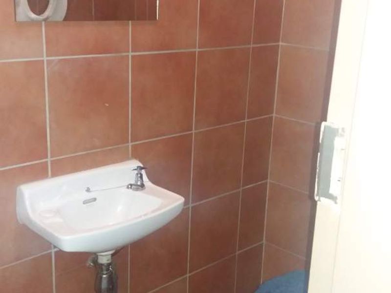 A compact guest bathroom featuring terracotta-style wall and floor tiles, a wall-mounted basin, and a standard toilet.