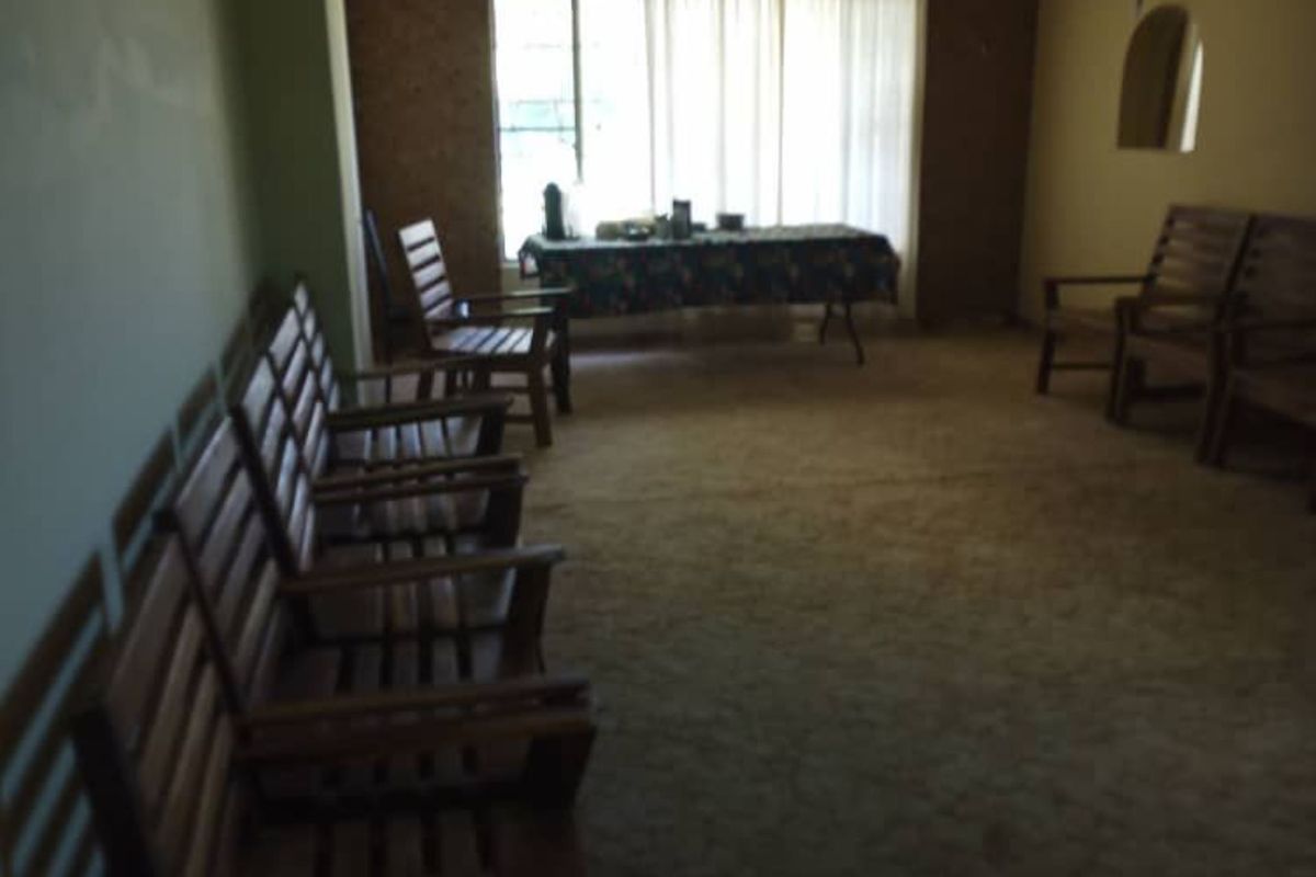 A spacious living area featuring wall-to-wall carpeting, a ceiling fan, and large windows allowing natural light into the room.