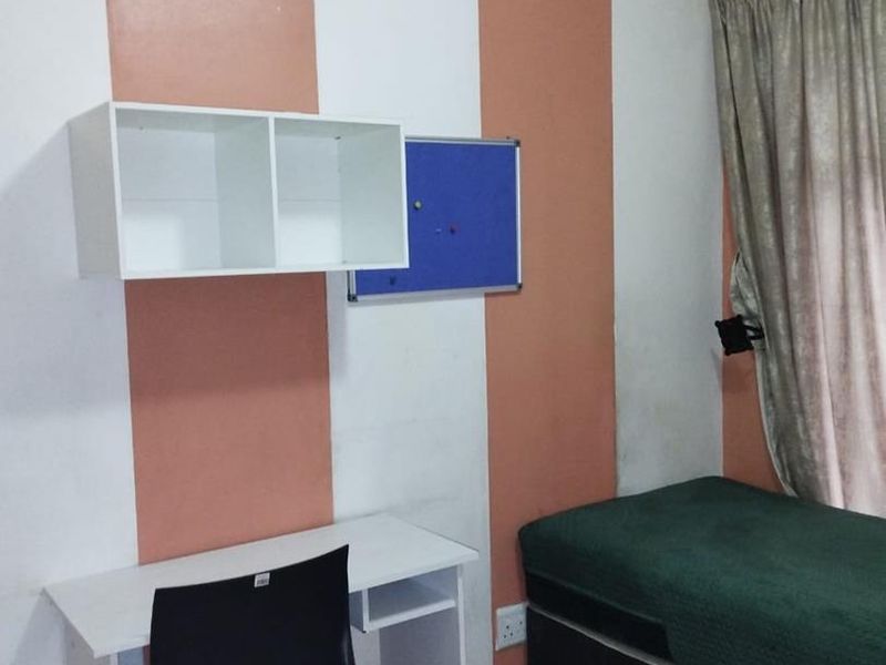 A compact bedroom featuring laminate flooring and vertical striped wall paint, providing a functional space for a single bed and study area.