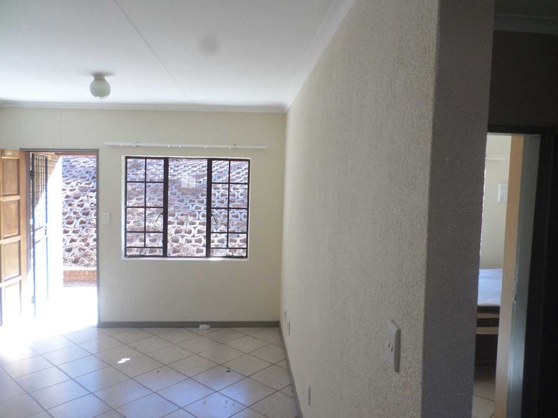 An empty living area featuring tiled flooring, textured walls, and a security gate leading to the exterior.