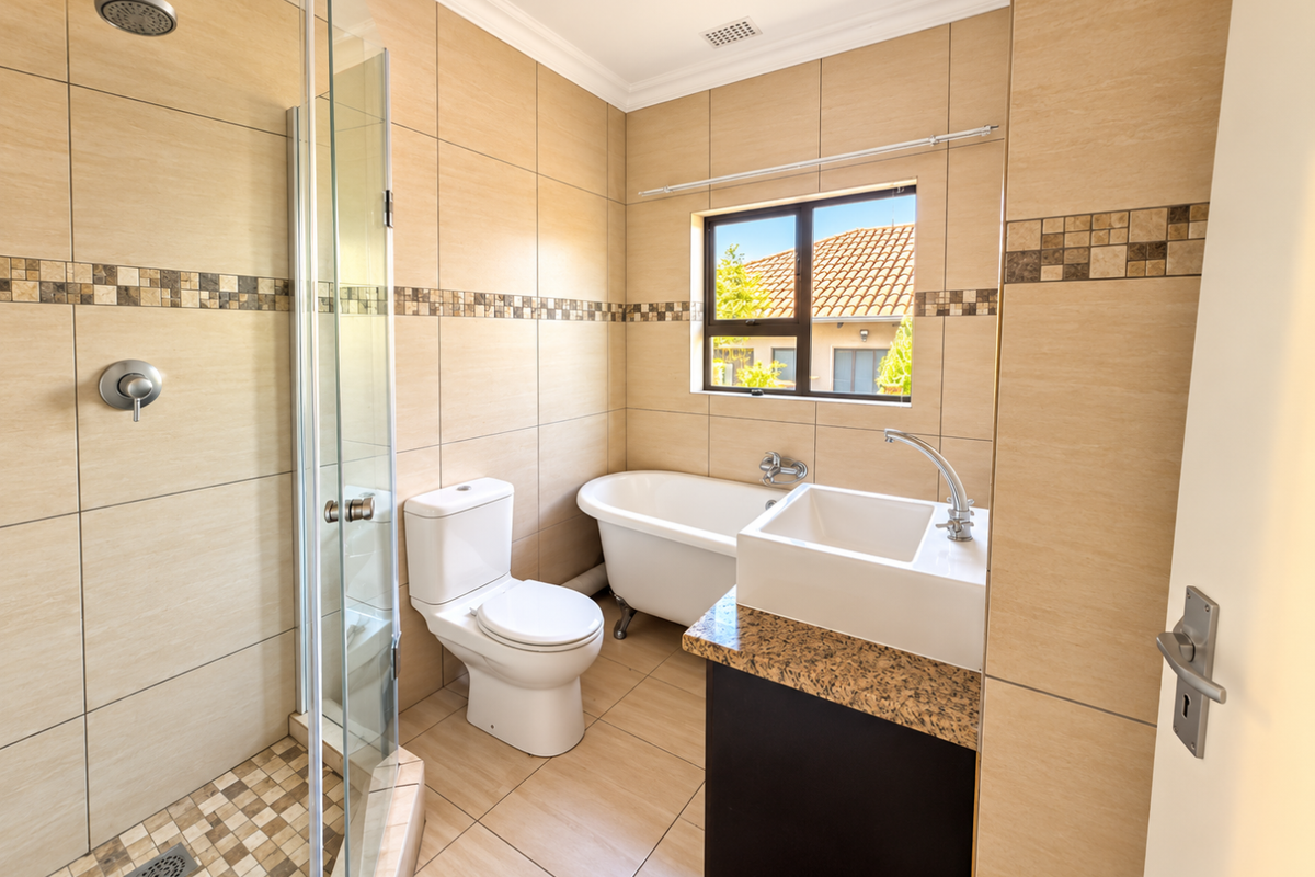 A well-maintained bathroom featuring a glass-enclosed shower, a classic freestanding bathtub, a modern vanity with granite countertop, and neutral floor-to-ceiling tiling.