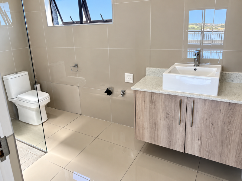 Modern bathroom featuring a wall-mounted wood-finish vanity with a vessel sink, stone countertop, glass shower screen, and neutral floor-to-ceiling wall tiles.