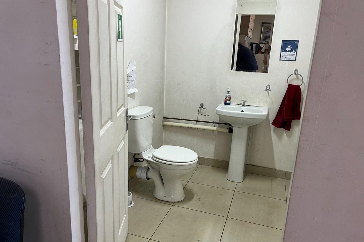 A functional commercial restroom featuring a standard pedestal basin, toilet, and wall-mounted mirror with tiled flooring.