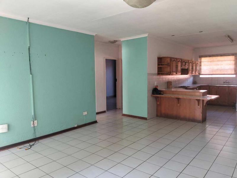 Open-plan living and kitchen area featuring tiled flooring, wooden cabinetry, and a breakfast bar, offering a functional layout ready for modernization.