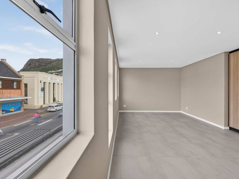A bright, empty bedroom featuring modern tiled flooring, recessed downlights, and a built-in wardrobe, offering a pleasant street view through large windows.
