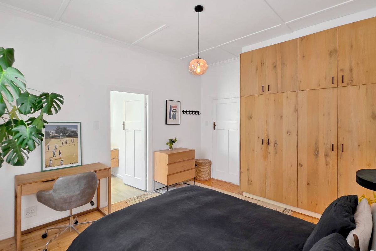 A well-maintained bedroom featuring warm hardwood flooring, a large built-in wooden wardrobe, and a classic panelled ceiling with a modern pendant light.