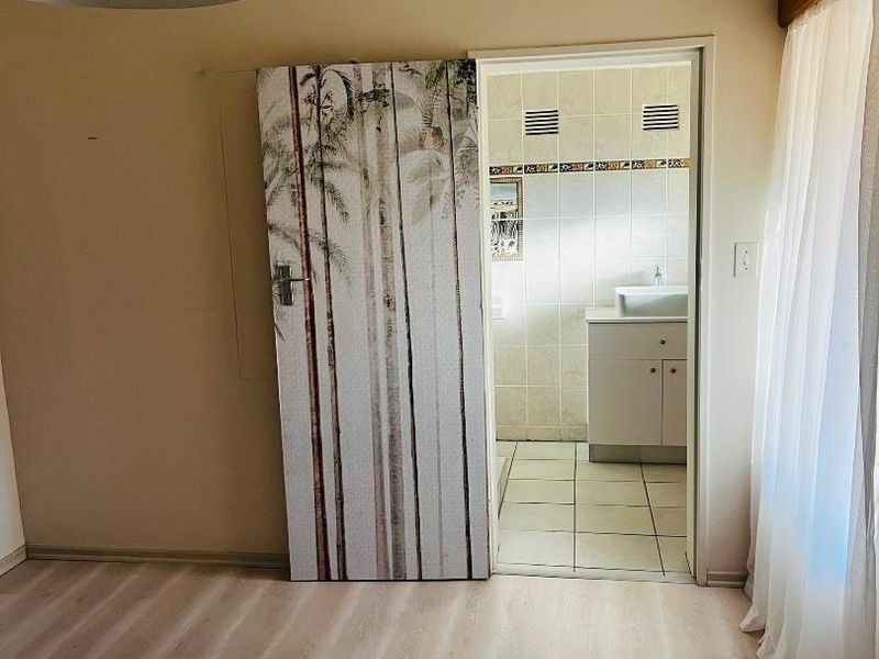 A bright, empty bedroom featuring light-toned laminate flooring and a pendant light, with direct access to an en-suite bathroom.