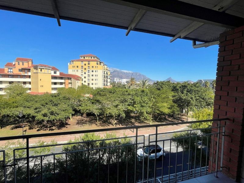 A covered balcony featuring a metal railing and exposed brickwork, offering scenic views of the surrounding neighborhood and mountain landscape.