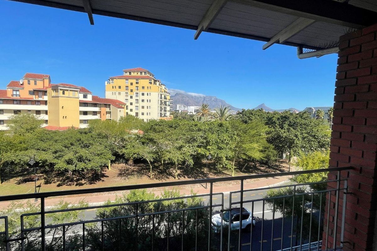 A covered balcony featuring a metal railing and exposed brickwork, offering scenic views of the surrounding neighborhood and mountain landscape.