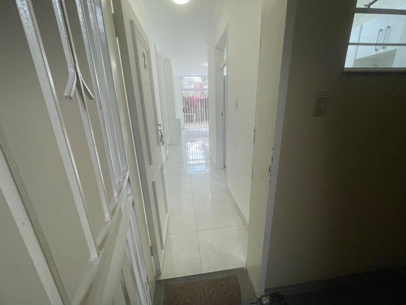 A bright, tiled hallway providing access to multiple rooms, featuring a secure metal gate at the end leading to an outdoor area.