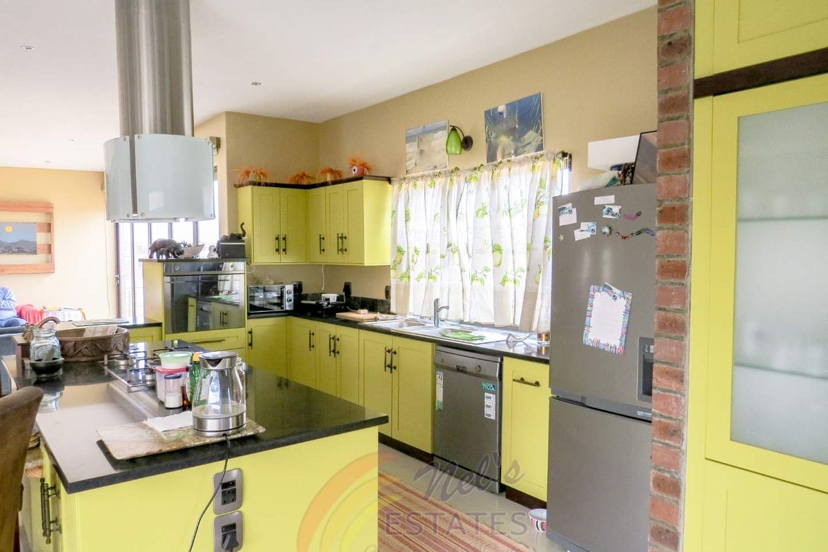 A kitchen featuring lime green cabinetry, dark granite countertops, a central island with a built-in hob, and a stainless steel extractor fan.