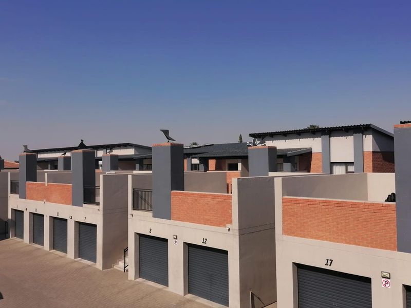 A view of the townhouse complex exterior, featuring multiple garage units with roller shutter doors and modern brick and plaster facade finishes.