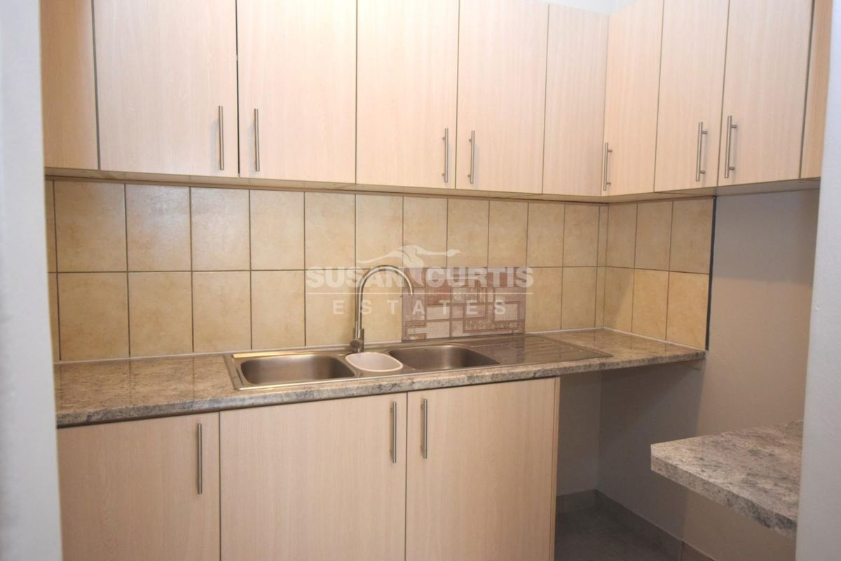 A functional kitchen area featuring light wood-tone cabinetry, stone-look laminate countertops, a double bowl stainless steel sink, and neutral ceramic tile backsplash.