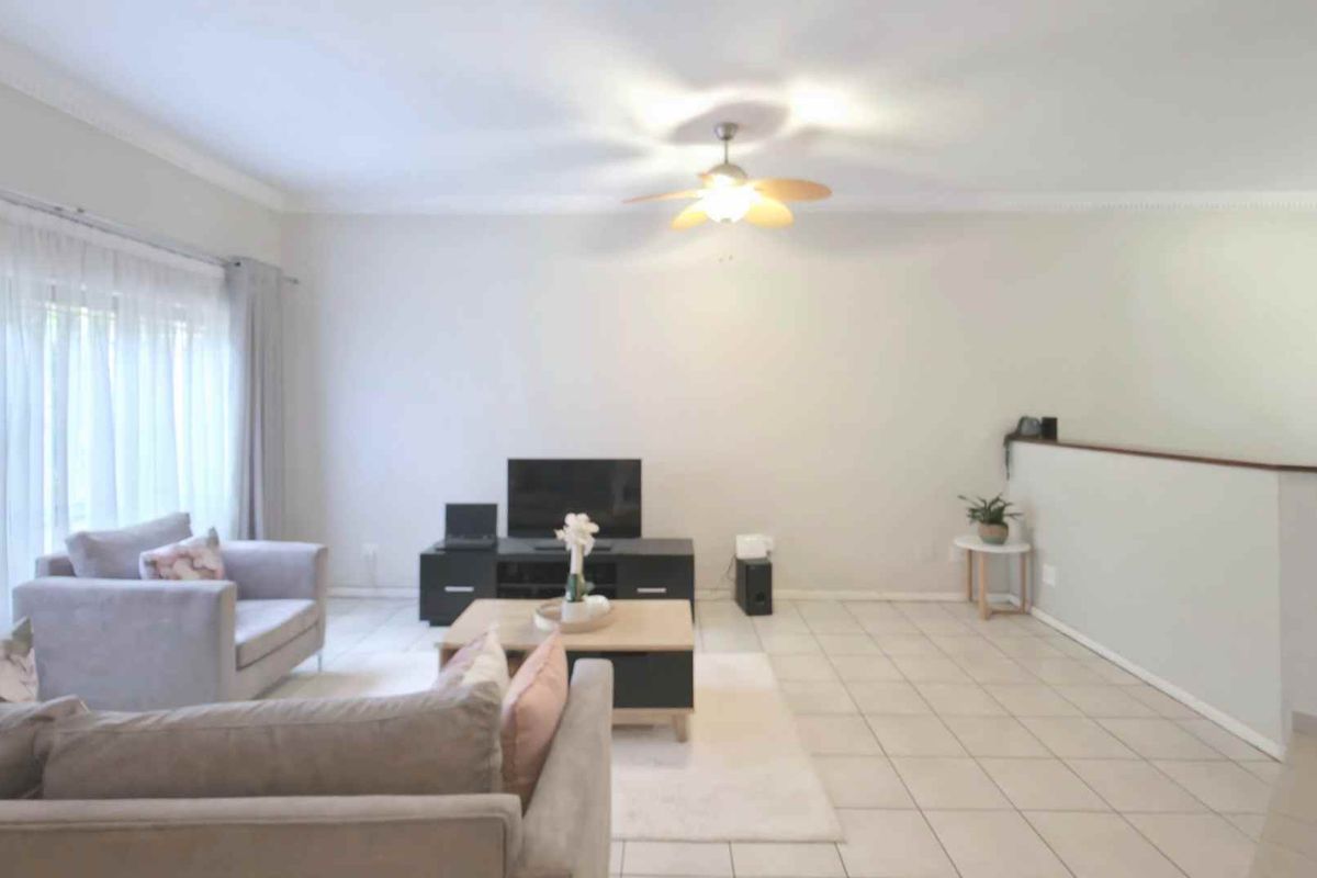 A spacious living room featuring neutral tiled flooring, a ceiling fan, and a half-wall partition, offering a bright and open layout.