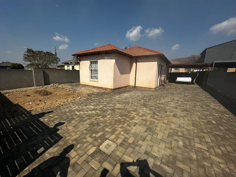 Rear view of the property featuring a paved driveway, carport, and a tiled roof house with a surrounding boundary wall.